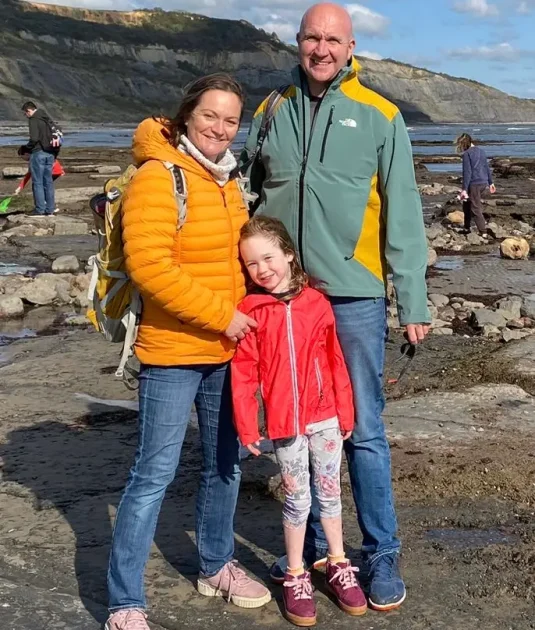 photograph of a family, a man, woman and their daughter standing on a beach in coats